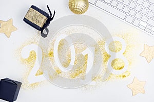 Luxury glowing numbers 2018 made from gold shiny glitter on white table with keyboard and christmas decoration.