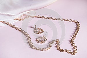 Luxury gold jewelry chain and earrings on pink background with silk, copy space, selective focus