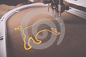 A luxury golden ox symbol is stitched on brownish shiny olive fabric by an modern embroidery machine