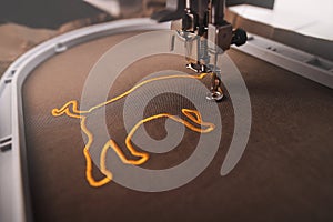 A luxury golden ox symbol is stitched on brownish shiny olive fabric by an modern embroidery machine in enigmatic light.