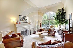 Luxury high ceiling living room interior with fireplace, leather sofas and arched window.