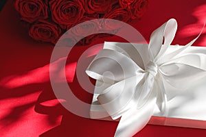 Luxury holiday silk gift box and bouquet of roses on red background, romantic surprise and flowers as birthday or Valentines Day