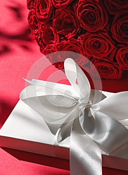 Luxury holiday silk gift box and bouquet of roses on red background, romantic surprise and flowers as birthday or Valentines Day