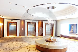 Luxury hotel lobby or hall with three modern elevators and glass chandelier in the middle