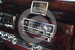 Luxury interior of old classic American car. Wooden decorated dashboard with radio and clocks.