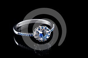 Luxury jewellery. White gold or silver engagement ring with colored gemstone closeup on black background. Selective focus.