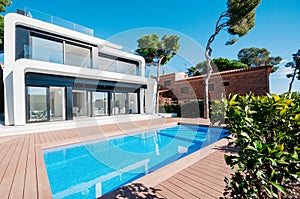 Luxury modern white house with large windows overlooking a Mediterian landscaped garden with palm trees and  blue swimming pool.