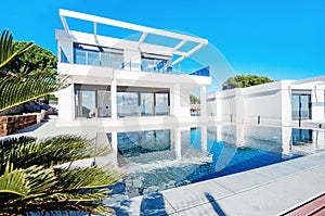 Luxury modern white house with large windows overlooking a Mediterian landscaped garden with palm trees and  blue swimming pool.