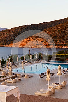 Luxury morning swimming pool with empty deck chairs, tables and umbrellas at the resort with beautiful sea view. Greek