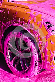 Luxury orange car on self servise car washing. Pink foam on auto. Close-up of wheels