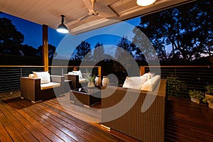 Luxury outdoor lounge area with chairs and cushions looking onto beautiful garden from a deck, shot at twilight