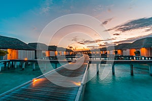 Luxury over water villas warm orange led lights, bungalows sea ocean with beach at night sunset time