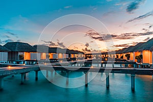 Luxury over water villas warm orange led lights, bungalows sea ocean with beach at night sunset time