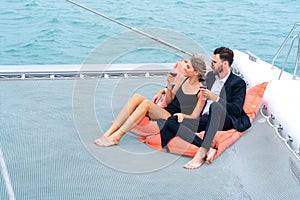 Luxury relaxing couple traveler in nice dress and suite sit on bean bag and drink a glass of wine in part of cruise yacht with