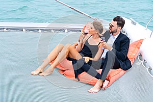 Luxury relaxing couple traveler in nice dress and suite sit on bean bag and drink a glass of wine in part of cruise yacht with