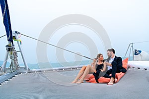 Luxury relaxing couple traveler in nice dress and suite sit on bean bag and drink a glass of wine in part of cruise yacht with