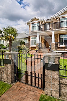 Luxury residential house with palm tree on the front yard behind metal fence.