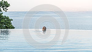 Luxury resort with infinity edge pool and a man traveler in lying down in swimming pool water enjoying summer holiday