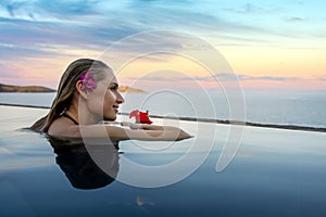 Luxury resort vacation - woman with flower in the hair relaxing in infinity swimming pool with sea view