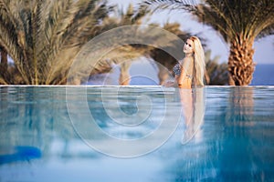 Luxury Resort. Woman Relaxing In Infinity Swimming Pool Water. Beautiful Happy Healthy Female Model Enjoying Summer Travel Vacatio