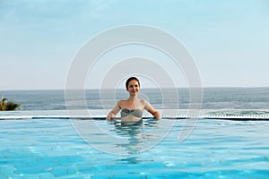 Luxury Resort. Woman Relaxing In Infinity Swimming Pool Water. Beautiful Happy Healthy Female Model Enjoying Summer Travel Vacatio