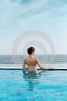 Luxury Resort. Woman Relaxing In Infinity Swimming Pool Water. Beautiful Happy Healthy Female Model Enjoying Summer Travel Vacatio