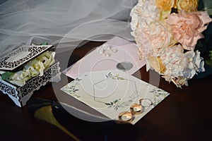 Luxury set of wedding invitations, wedding rings, earings and bridal bouquet on wood brown background.