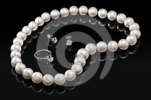 Luxury set white pearl necklace and jewelry with diamonds in ring and earrings on a black background with glossy reflection