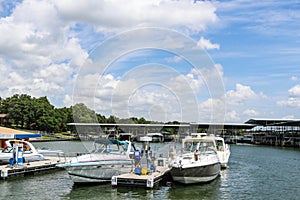 Luxury speedboats fueling up at gas pump at marina on lake with docks and boats behind under beautiful blue cloudy sky