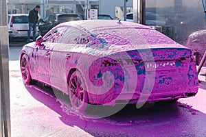 Luxury sport blue car on self servise car washing. Pink foam on auto. Back view