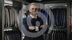 In the luxury suit shop client young Caucasian man with a cute smile looking to the camera posing and crossing hands and