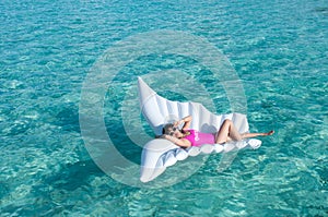 Luxury summer vacation beach woman relaxing lying down on inflatable pool float floating at Maldives sun tanning. Model sleeping o