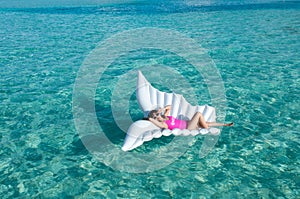 Luxury summer vacation beach woman relaxing lying down on inflatable pool float floating at Maldives sun tanning. Model sleeping o