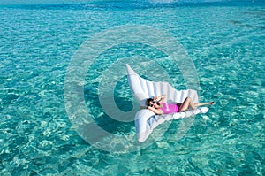 Luxury summer vacation beach woman relaxing lying down on inflatable pool float floating at Maldives sun tanning. Model sleeping o