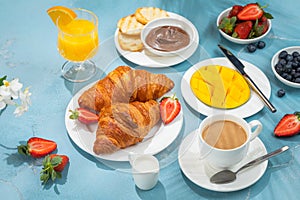 Luxury sunny continental breakfast on blue concrete background table with tropical plants shadows