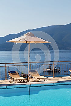 Luxury swimming pool with empty deck chairs and umbrella at resort with beautiful sea view