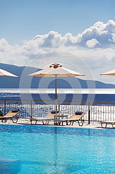 Luxury swimming pool with empty deck chairs and umbrellas at the resort with beautiful sea view