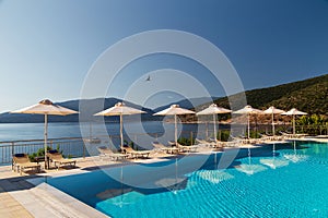 Luxury swimming pool with empty deck chairs and umbrellas at resort with beautiful sea view. Greek islands.