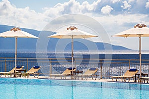 Luxury swimming pool with empty deck chairs and umbrellas at the resort with beautiful sea view