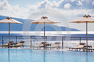 Luxury swimming pool with empty deck chairs and umbrellas at the resort with beautiful sea view