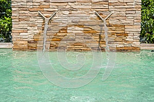 Luxury Swimming pool with a small waterfall fountain. Modern fountain detail. Waterfall drop design with decorative beige wall