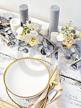 Luxury table setting in marine style with candles, mussels shells and grey-blue toned napkins.