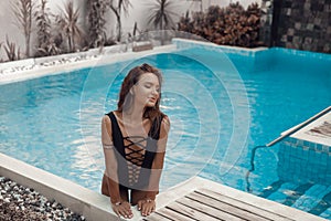 Luxury travel bikini girl with sexy body in black swimwear posing by swimming pool at luxurious villa. High fashion colors,