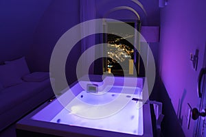 Luxury travel Santorini vacation hotel jacuzzi in colored lights with night view of the city.