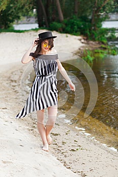 Luxury travel woman in black and white beachwear walking taking a stroll on sand summer beach. Girl tourist on summer