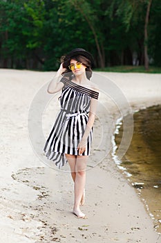 Luxury travel woman in black and white beachwear walking taking a stroll on sand summer beach. Girl tourist on summer