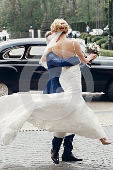 Luxury wedding couple dancing at old car in light. stylish bride and groom hugging and embracing in city street. romantic