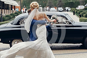 Luxury wedding couple dancing at old car in light. stylish bride and groom hugging and embracing in city street. romantic