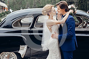 Luxury wedding couple dancing at old car in light. stylish bride and groom hugging and embracing in city street. romantic