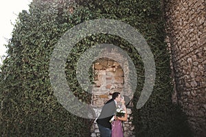 Luxury wedding couple hugging and kissing on the background gorgeous plants, cave near ancient castle